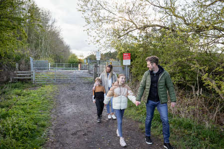 A front-view shot of a caucasian mother and father walking with their son and daughter, they're holding hands and smiling after walking past a level crossing railroad.の写真素材