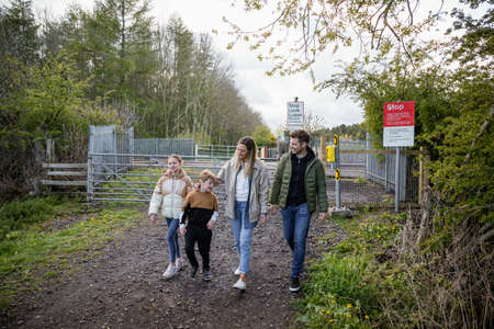 A front-view shot of a caucasian mother and father walking with their son and daughter, they're holding hands and smiling after walking past a level crossing railroad.の写真素材