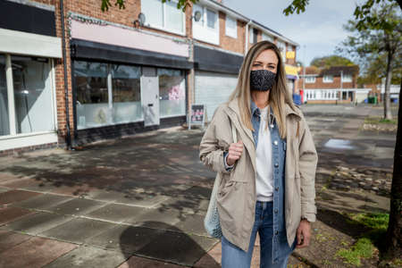 A front-view wide-view portrait shot of a mid-adult caucasian woman wearing casual clothing, she's smiling and looking at the camera. She is also wearing a protective face mask to help stop the spreadの写真素材
