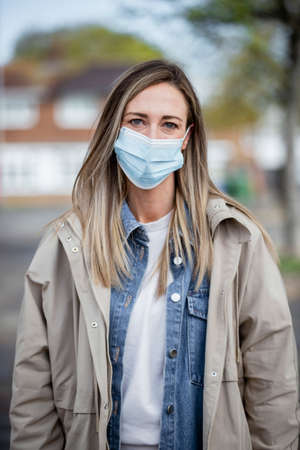 A front-view portrait shot of a mid-adult caucasian woman wearing casual clothing, she's smiling and looking at the camera. She is also wearing a protective face mask to help stop the spreadの写真素材