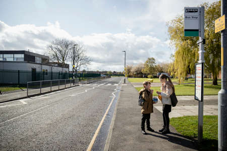A shot of a young brother and sister standing on a street pathway, they are waiting at a bus stop...