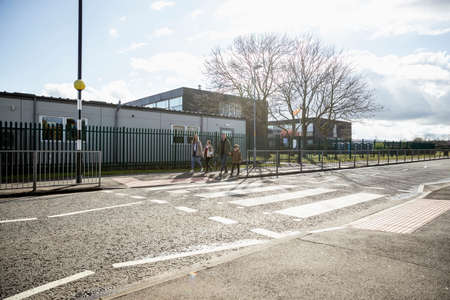 A shot of a four person family crossing the road safely at a zebra crossing, the parents are taking their children home from school.の写真素材