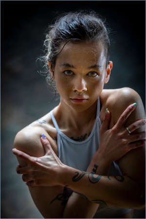 A young woman with tattoos in sports clothing, she is embracing herself with her arms on her chest. She is looking at the camera.の写真素材