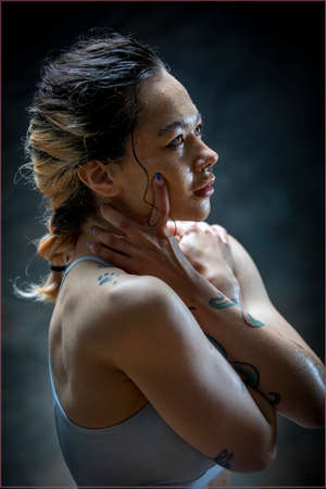 Side view of a young woman with tattoos in sports clothing, her head is resting on her arms. She is looking up while sweat travles down her face.の写真素材