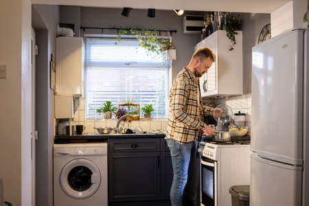 A side-view shot of a caucasian man standing in his kitchen, he is making pasta for lunch.の写真素材