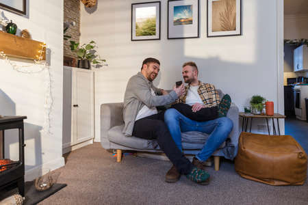 A front-view shot of an LGBTQI same sex male couple sitting in their living room relaxing, one man is showing his partner his smart phone.の写真素材