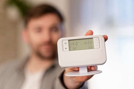 A front-view shot of a man holding up a gadget in his home.の写真素材