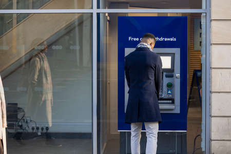 Man using cash machine to withdraw money on high streetの写真素材