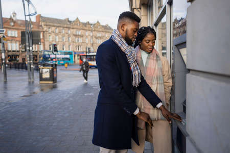 Couple standing by atm withdrawing moneyの写真素材