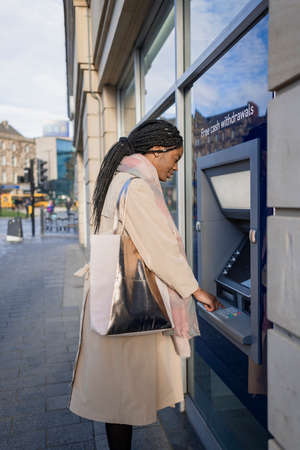 Woman with braided ahir standing at cash machine withdrawing moneyの写真素材
