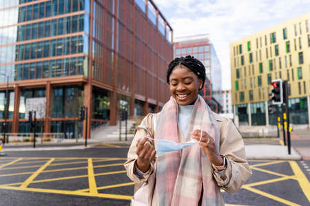 Woman smiling and holding face covering by road with buildings on background in cityの写真素材