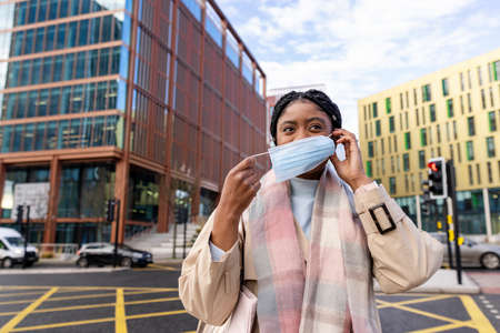 Woman holding elastic and placing face covering over nose and mouthの写真素材