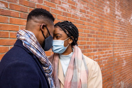 Couple wearing face masks facing each other by brick wallの写真素材