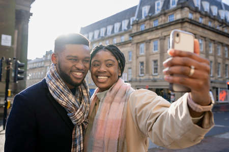 Cheerful couple in town, woman holding phone taking selfieの写真素材