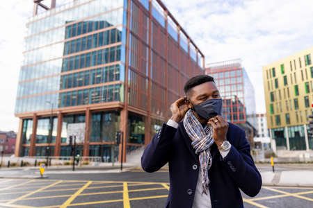 Man standing by road adjusting face mask with buildings in backgroundの写真素材