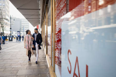 Cheerful couple walking arm in arm past the shops in townの写真素材