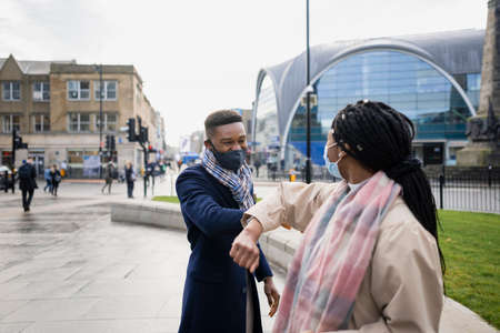 Friends meeting in city centre with face coverings, touching elbows during pandemic, social distancingの写真素材