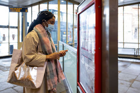 Woman with face covering holding phone and looking at bus timetableの写真素材