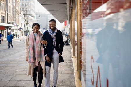 Cheerful couple in town walking arm in arm past shop frontの写真素材