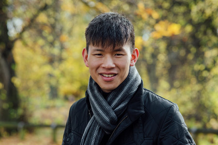 A portrait of a young, Chinese man standing outdoors in nature in Northumberland, North East England during Autumn. He is smiling while looking at the camera.の写真素材