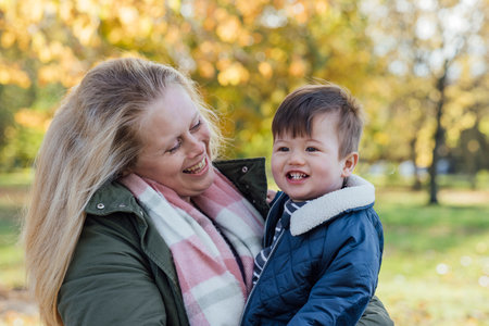 A mid adult woman carrying her baby boy in her arms while standing outside and embracing him in nature in Northumberland, North East England. The woman is looking at her son wihle they both smile.の写真素材