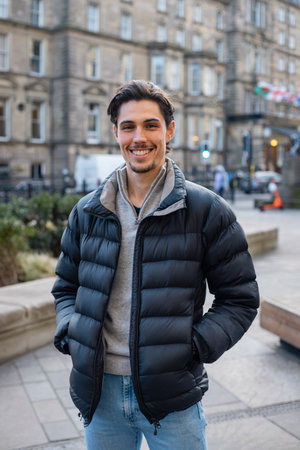 A young man spending the day in Newcastle Upon Tyne. He is standing on a paved area in the city centre with buildings behind him. He is looking at the camera and smiling.の写真素材