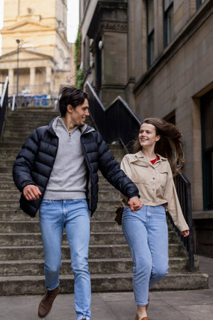 A young couple spending the day in Newcastle Upon Tyne together. They are holding hands and running through the city with steps behind them.の写真素材