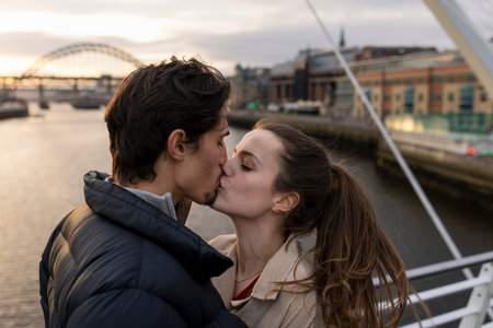A close-up shot of a young couple standing side by side sharing a kiss together on a bridge in the city, they are in love.の写真素材