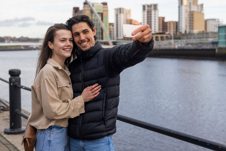 A wide-view shot of a young couple standing together taking a selfie, they are in love.の写真素材