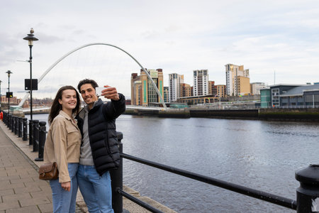 A wide-view shot of a young couple standing together taking a selfie, they are in love.の写真素材