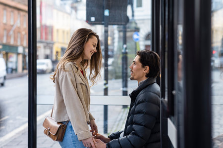 A side-view shot of a young couple waiting at a bus stop together, they are in love.の写真素材
