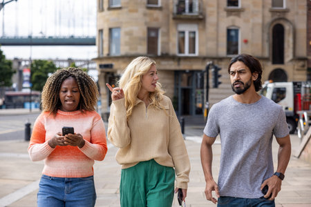 Wide shot of three mid adult friends standing in a city street in Newcastle, England. They are looking for directions while using a smartphone. They are discussing which way to go.の写真素材