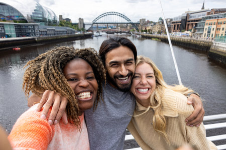 Front-view selfie shot of three mid adult friends standing on a bridge in Newcastle, England. They are smiling and looking at the camera while taking a group selfie.の写真素材