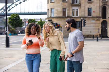 Wide shot of three mid adult friends standing in a city street in Newcastle, England. They are looking for directions while using a smartphone.の写真素材