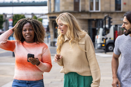 Wide shot of three mid adult friends standing in a city street in Newcastle, England. They are looking for directions while using a smartphone. They are discussing which way to go.の写真素材