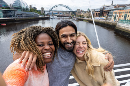Front-view selfie shot of three mid adult friends standing on a bridge in Newcastle, England. They are smiling and looking at the camera while taking a silly group selfie.の写真素材