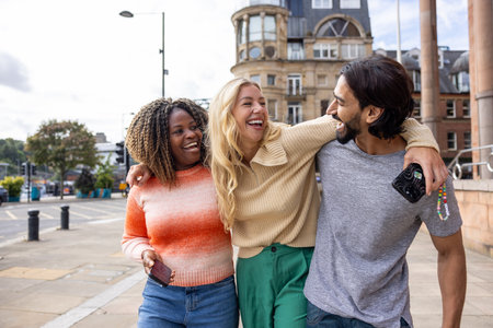 Wide shot of three mid adult friends standing in a city street in Newcastle, England. They are looking for directions while using a smartphone, and their arms are around eachother.の写真素材