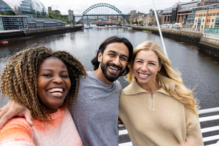 Front-view selfie of three mid adult friends standing in a city centre, on a bridge in Newcastle, England. They are smiling and looking at the camera while taking a group selfie.の写真素材