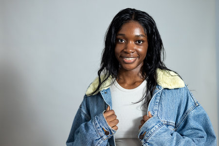 Waist-up studio portrait of a young adult female smiling at the camera. She is wearing casual clothing, standing against a neutral studio background.の写真素材
