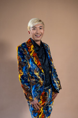 Studio shot of a young adult male smiling at the camera. He has bleached hair and is wearing a...