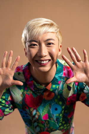 Studio shot of a young adult male reaching towards the camera happily. He has bleached hair and is...