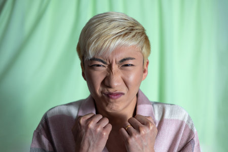 Studio shot of a young adult male making a face to the camera with nose scrunched. He has bleached...