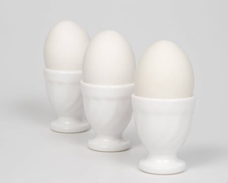 Three white eggs in glass eggcups on a white background.の写真素材