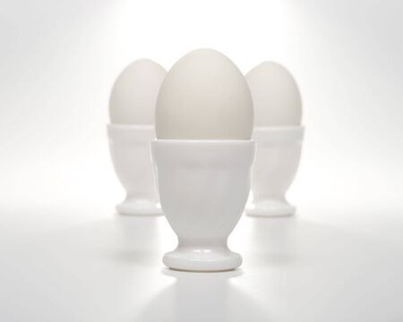 Three white eggs in glass eggcups on a white background. Selective focus.の写真素材