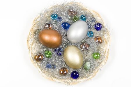 Gold, silver and bronze eggs in a basket with a glass stones. Isolated on a white background.