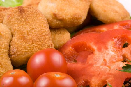 Appetizing fried chicken nuggets  with tomatoes, cucumber and pepper on salad leaves. Close-up. Selective focus.の写真素材