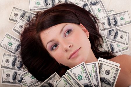 Portrait of the young beautiful woman lying on background from banknotesの写真素材