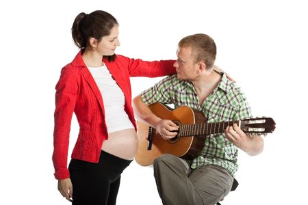 The young husband plays a guitar for the pregnant wife and the future child on a white background.の写真素材