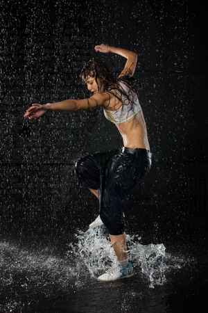 The beautiful girl dancing in water under rain on a black background.  Modern dances.の写真素材