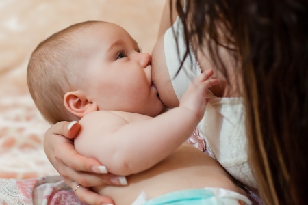 Young mum nurses the child on  on the house bed. Breastfeeding.
